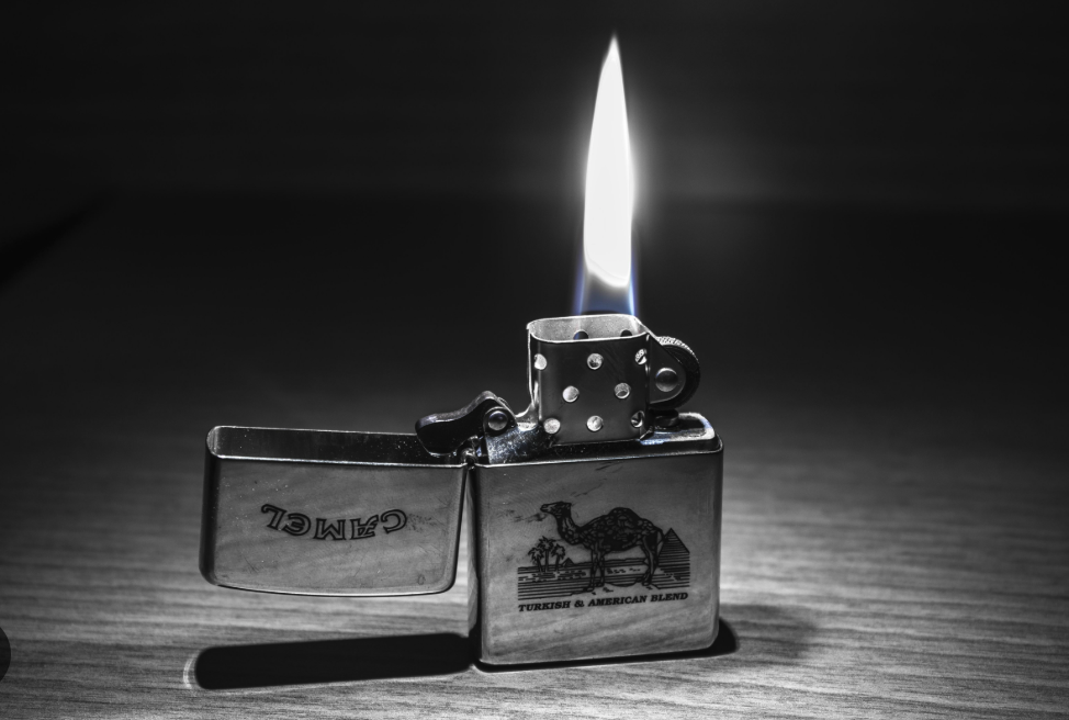 Metalni upaljač (ZIPPO stil) s plamenom na drvenoj podlozi